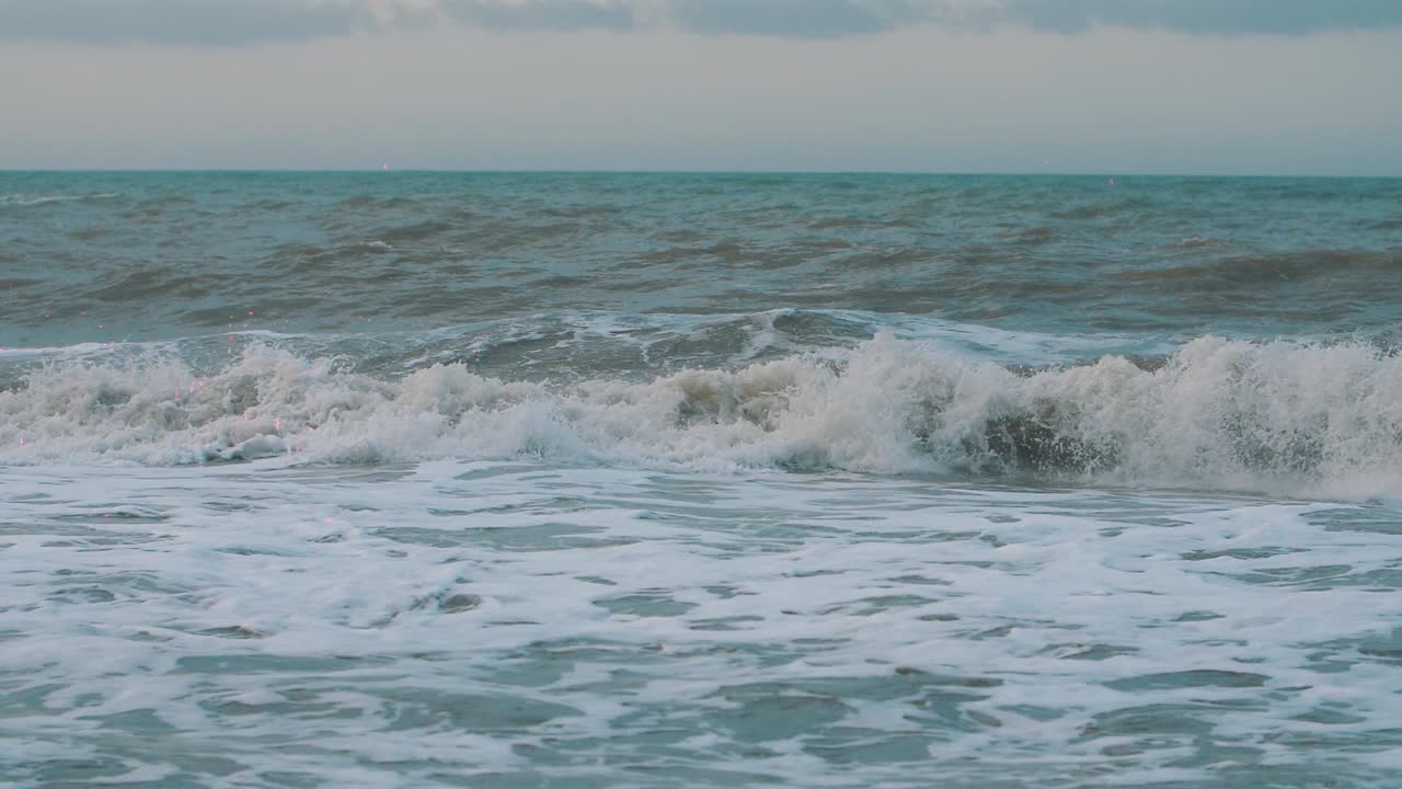 거품이 이는 파도가 움직이고, 충돌하고, 해변 해안에서 슬로우 모션으로 형성됩니다.