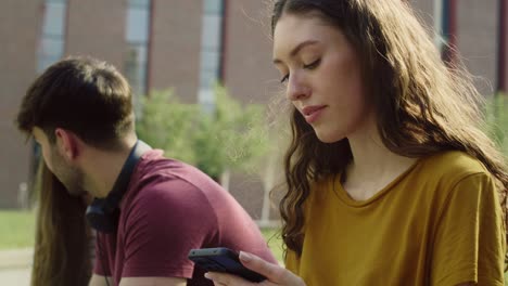 Caucasian-girl-browsing-phone-next-to-a-group-of-other-students