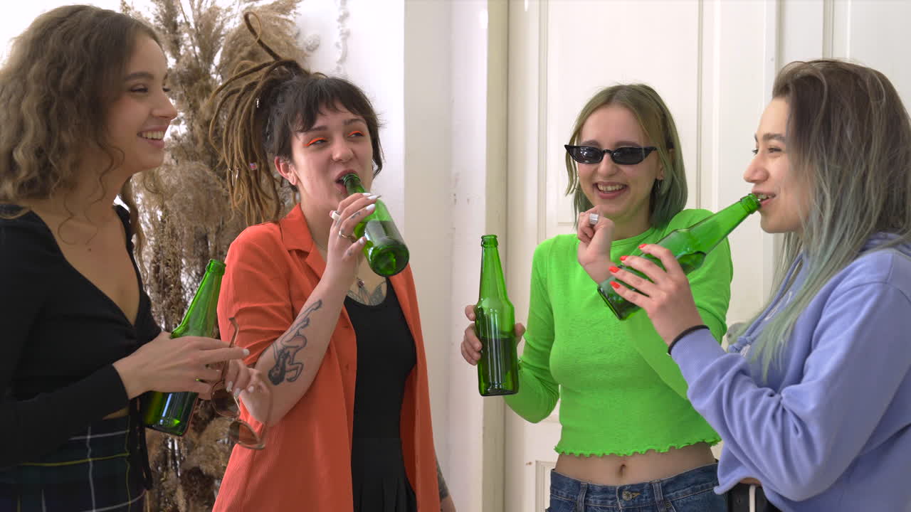 grupo de cuatro amigas felices bebiendo cerveza, hablando y bailando en casa
