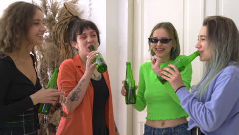 group of four happy girl friends drinking beer, talking and dancing at home