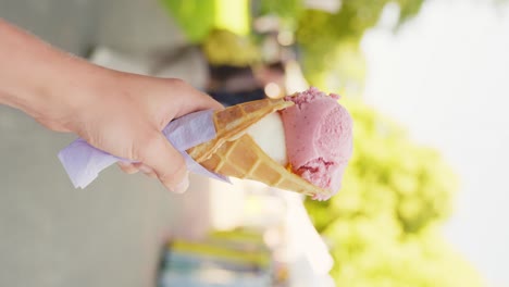 clip vertical de mano sosteniendo un helado de fresa y vainilla en la calle