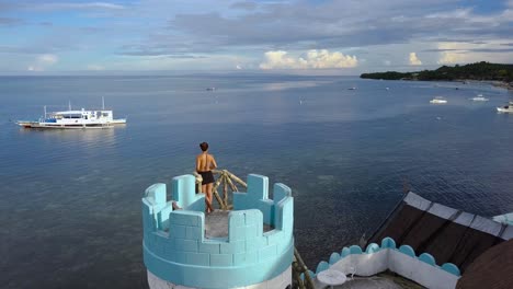 Woman-gazes-at-shoreline-in-Philippines-from-tower,-aerial-orbit-shot