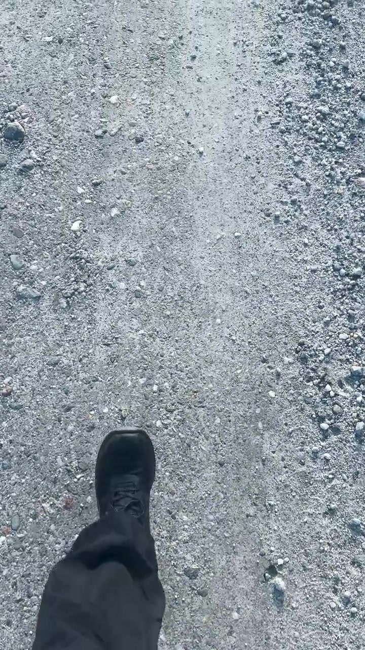 Bir kişi, çakıllı bir patikada sabit adımlarla yürüyor, gün ışığı, birinci şahıs bakış açısı, doğal dış ortam.