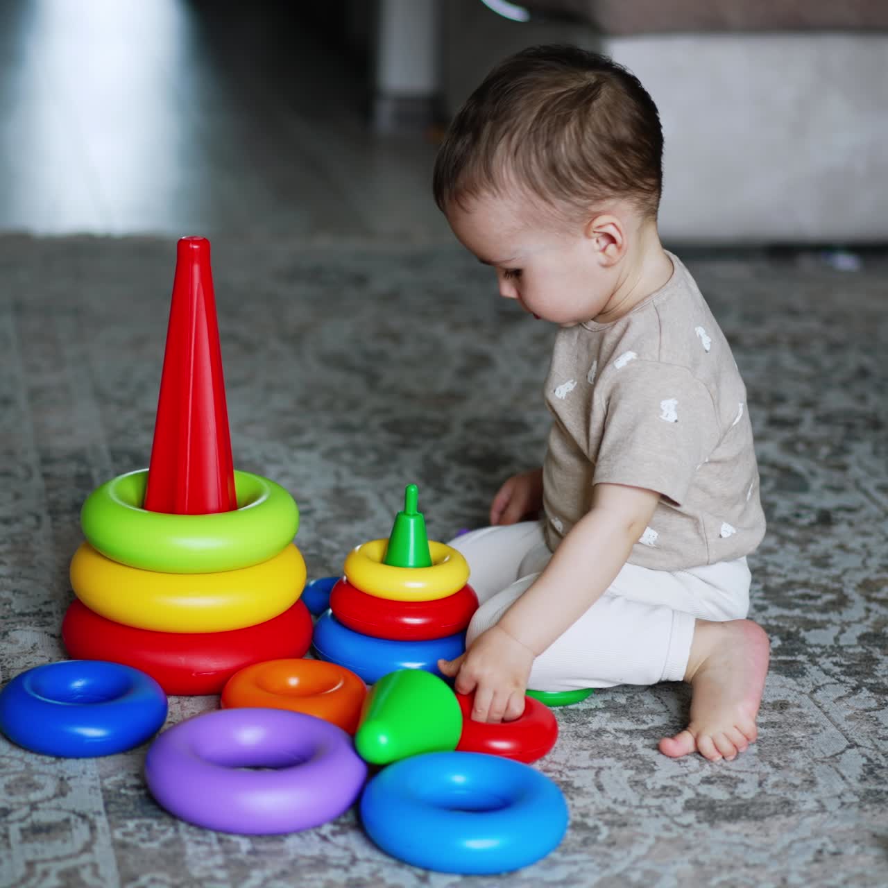 Smart little boy plays with his toys on the floor. Lovely baby assembling the pyramids. High angle view