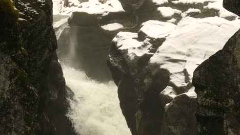 waterfall between large grey rocks, rapids cascading down, water under sunlight, natural light