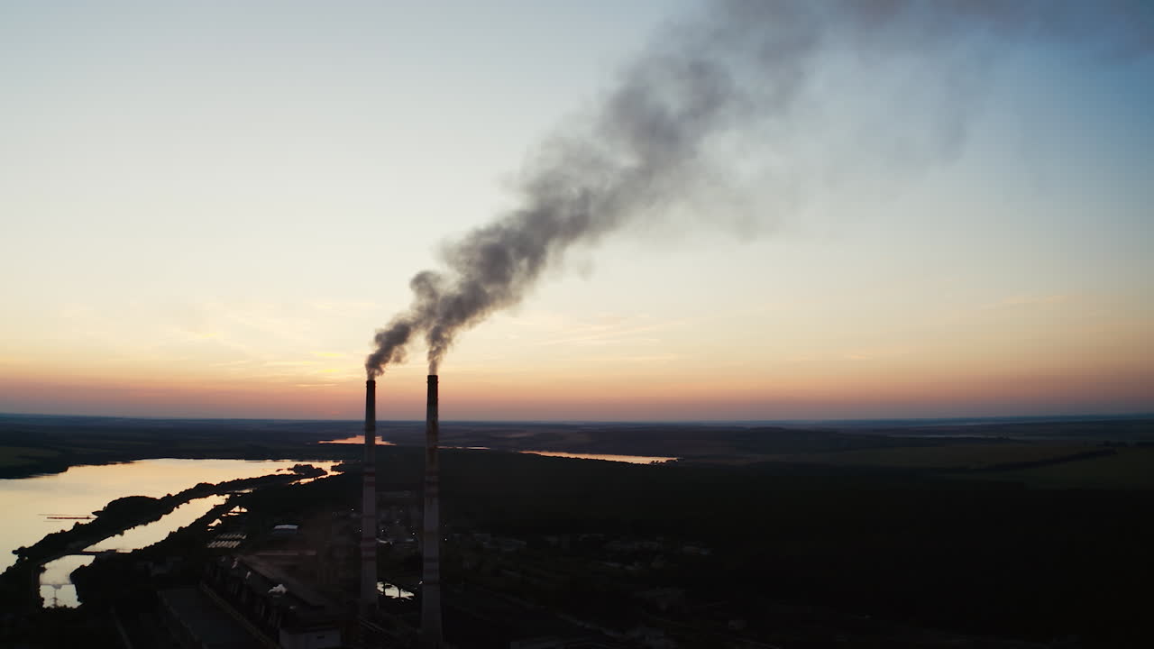 Ecological disaster. Dirty emissions from industrial pipes on the natural environment in the evening. Factory near the river at sunset.