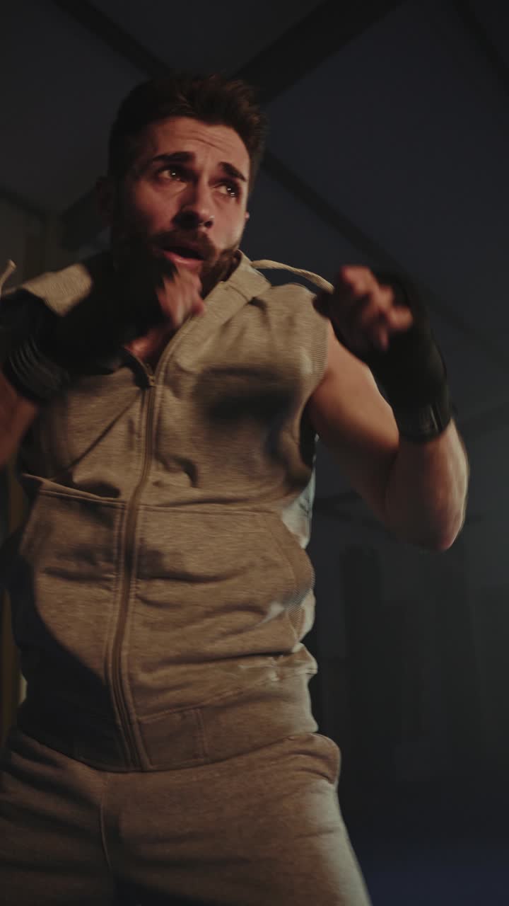 Uomo determinato che fa boxe a vuoto e si allena in una palestra buia
