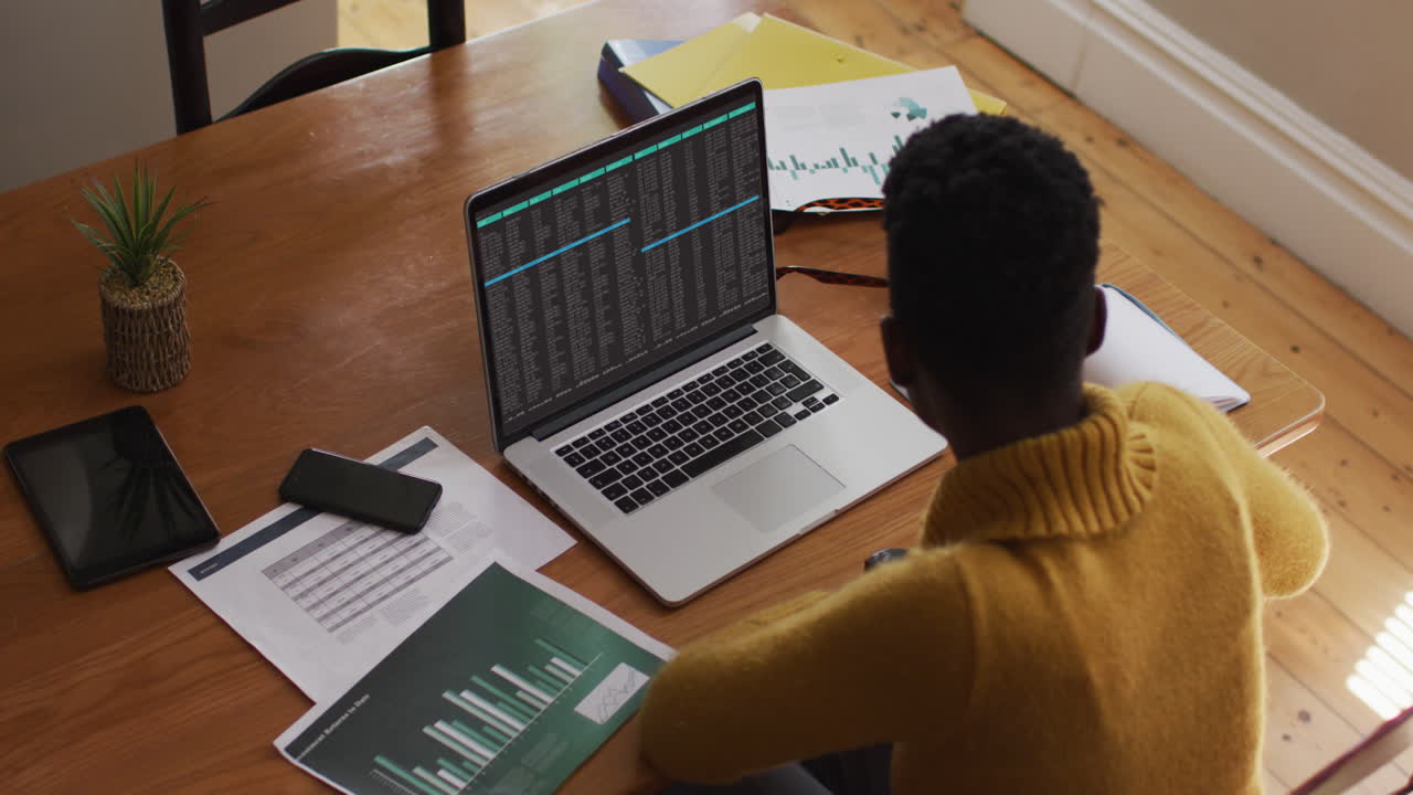 African american man sitting at desk coding data on laptop