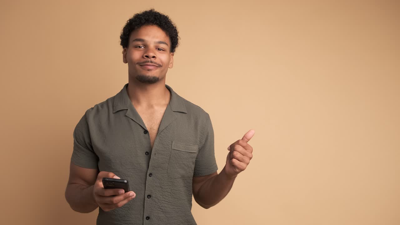 Glad mand bruger mobiltelefon og peger til siden i beige studie