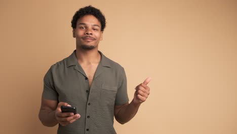 happy man using cellphone and pointing sideways in beige studio