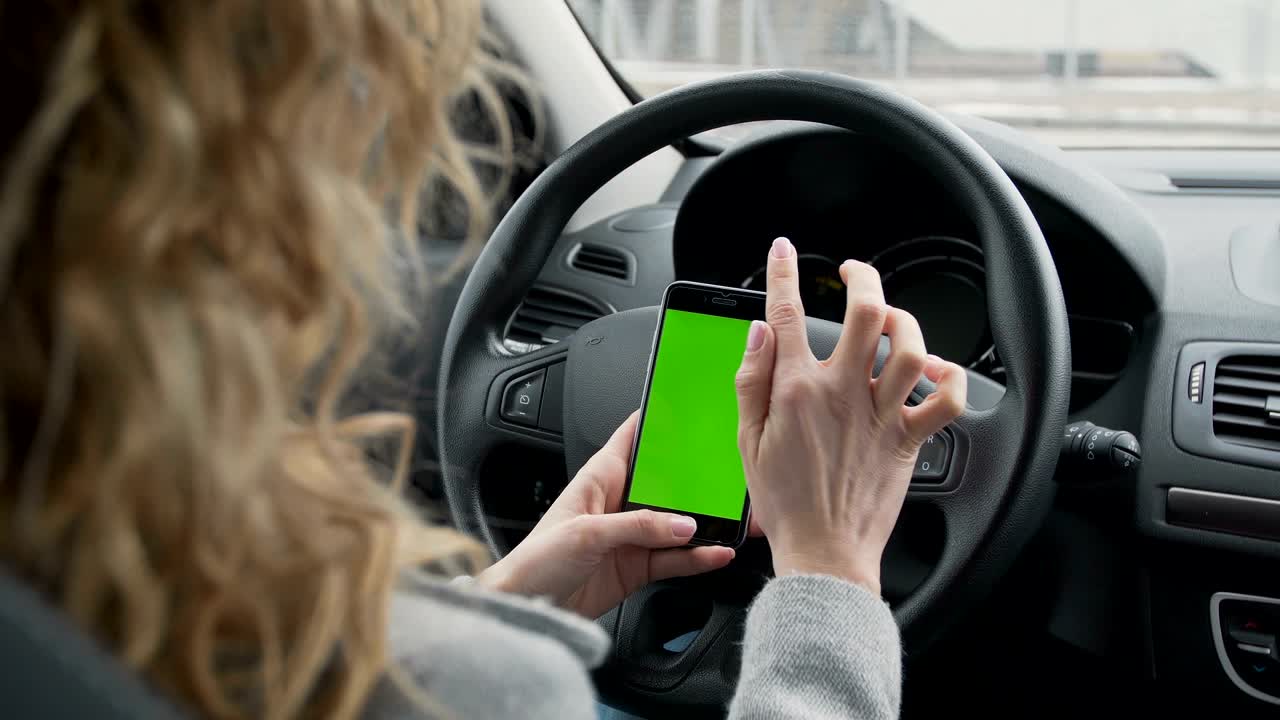 mujer se sienta en el coche moderno y trabaja en el teléfono inteligente - pantalla verde - primer plano