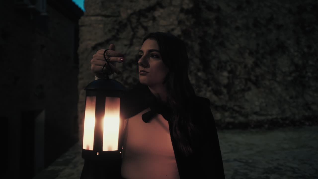 mujer misteriosa con linterna por la noche en la ciudad medieval
