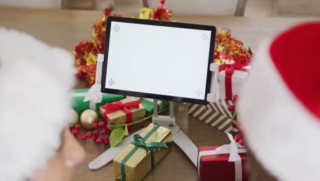 Video-Eines-Paares-Mit-Weihnachtsmützen-Und-Geschenken,-Das-Einen-Weihnachtsvideoanruf-Auf-Einem-Tablet-Mit-Kopierplatz-Macht