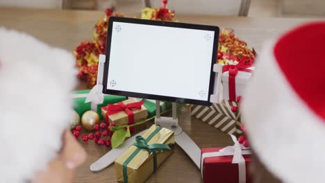 video de una pareja con sombreros de papá noel con regalos haciendo una llamada de video de navidad en una tableta con espacio para copiar.