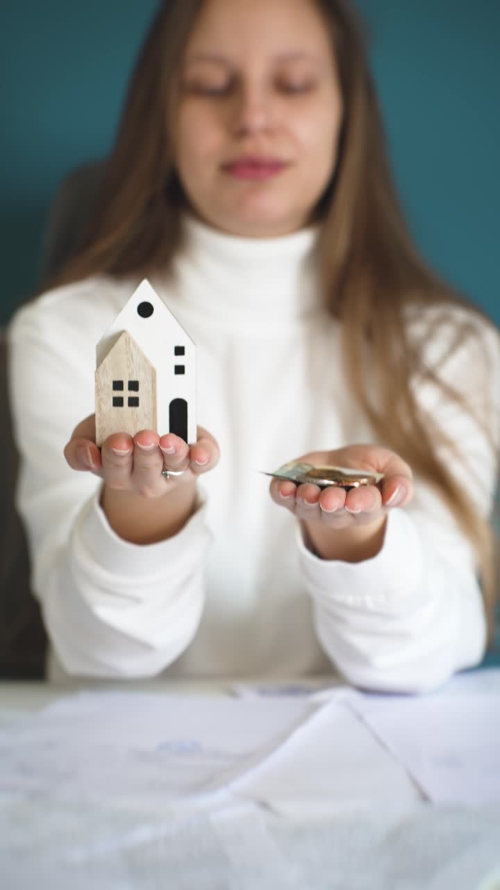 Donna che tiene denaro in una mano e una casa in miniatura nell'altra, a rappresentare decisioni finanziarie, risparmio e pianificazione per la futura proprietà di una casa
