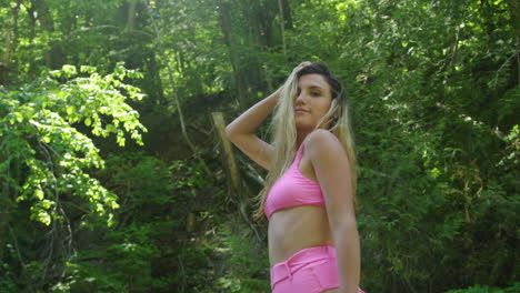 hot young woman poses and smiles, standing in a river surrounded by forest