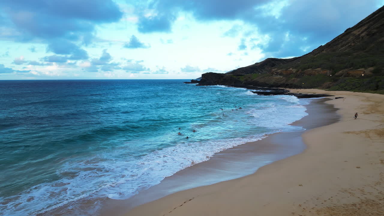 aérea sobre una playa de arena en oahu mientras la gente nada en las olas