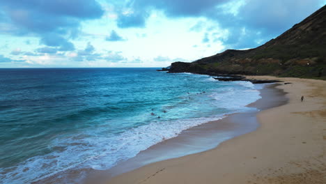 aerial over a sandy beach in oahu as people swim in the surf