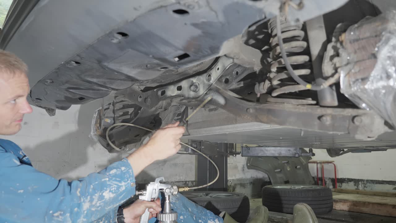 Man sprays automotive lanolin product on car rear crossmember, wheel suspension and support components