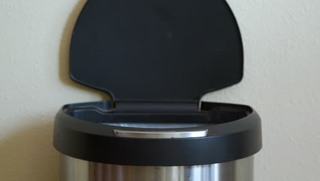man throws away yellow package in motion sensing touchless trash can - close-up