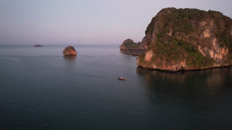 wide-aerial-circling-a-single-thai-longtail-boat-during-sunrise-near-Railay-Beach-in-Krabi-Thailand-around-the-beautiful-limestone-mountains-of-Krabi-Thailand-in-the-Andaman-Sea