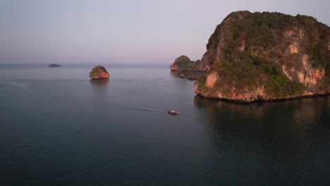 amplia antena que rodea un solo bote de cola larga tailandés durante el amanecer cerca de la playa de railay en krabi, tailandia, alrededor de las hermosas montañas de piedra caliza de krabi, tailandia, en el mar de andaman