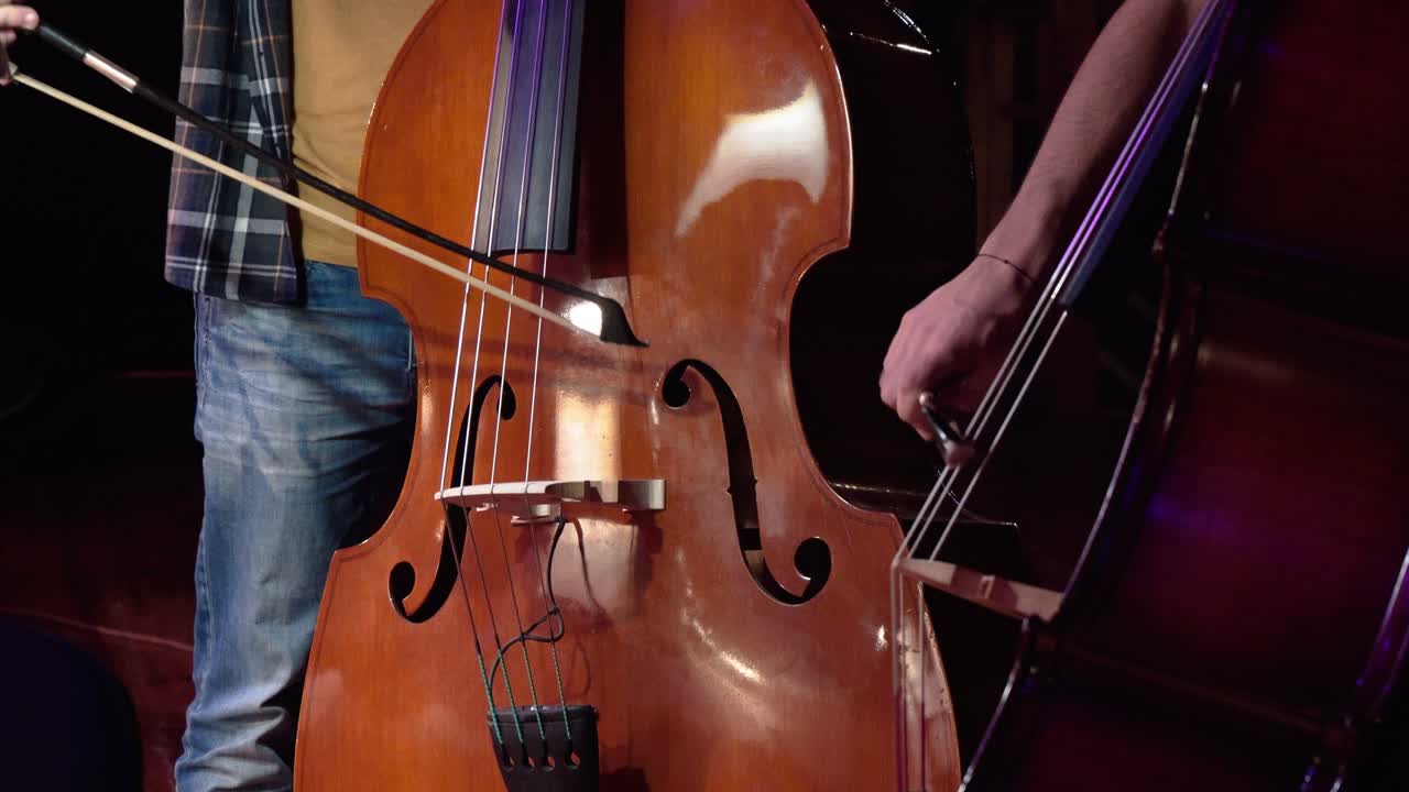 Two men in casual clothes playing the double bass in an orchestra