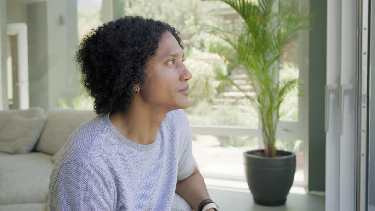 African American man sitting on light sofa by window seeing camera turning smiling laughing watch