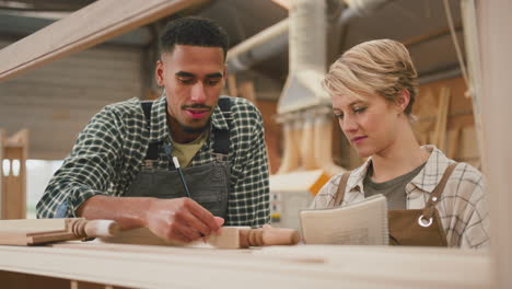 male and female apprentices working as carpenters in furniture workshop measure wood and take notes