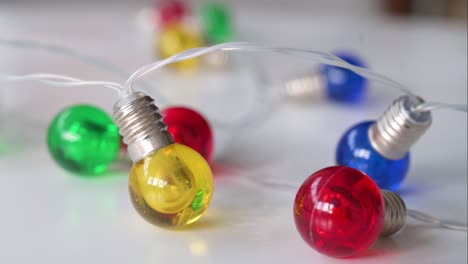 Examining-closely,-Christmas-LED-lights-in-blue,-red,-yellow,-and-green-against-a-white-backdrop