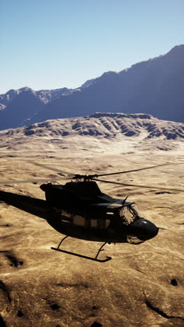 black helicopter flying over a desert landscape with mountains in the background