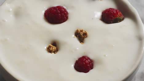 cereales de granola y bayas que caen en un cuenco blanco lleno de yogur