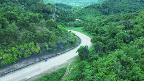 aerial drone footage following a moped driving on a country road in between green mountains in rural philippines