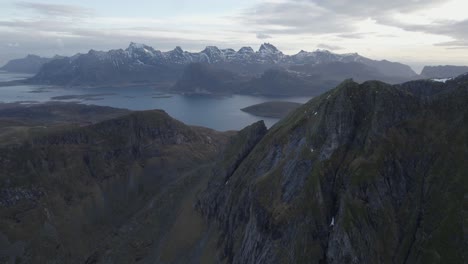 Vista-Aérea-De-Montañas-Empinadas-Con-Picos-Nevados-En-El-Fondo,-En-Lofoten,-Noruega---Marcha-Atrás,-Inclinación,-Disparo-De-Drones