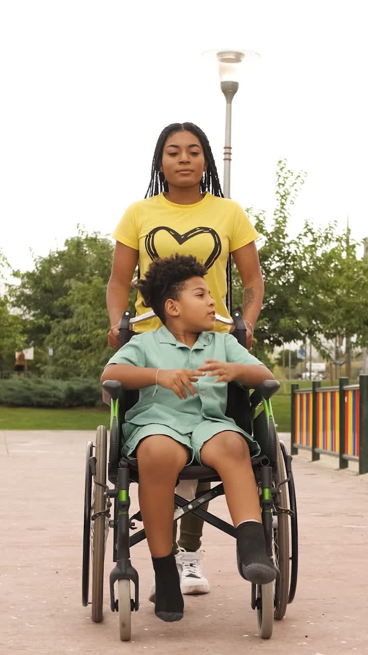 A woman assists a boy in a wheelchair in a park