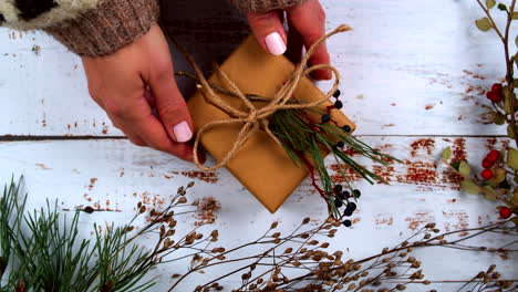 hands tying a rustic gift with natural twine, decorated with pine sprigs and berries. perfect for showcasing holiday gift-wrapping, diy, and nature-inspired seasonal aesthetics. flat lay top view.