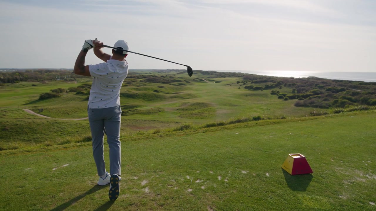 Golfer swing from tee at seaside golf course on sunny day