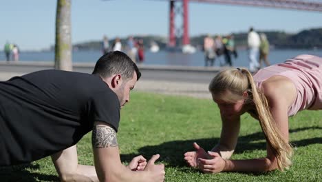 Sporty-young-couple-doing-exercises-on-green-meadow.