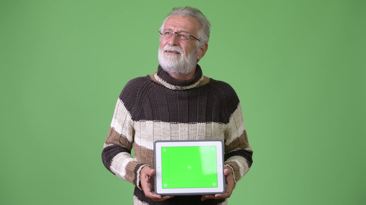 Homem idoso barbudo e bonito usando roupas quentes contra fundo verde.