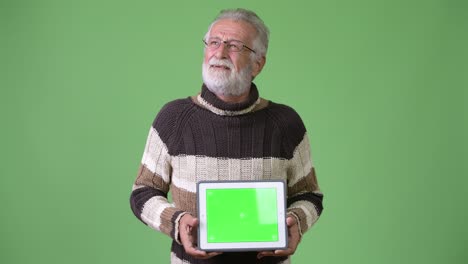 handsome senior bearded man wearing warm clothing against green background