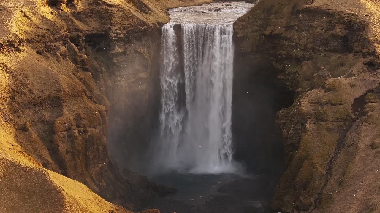 Iceland’s iconic Skógafoss waterfall from above, roaring falls, misty spray and golden cliff textures near Skógar and Eyjafjallajökull volcano.