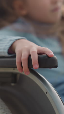 little girl sits in wheelchair with fair hair waving in wind on blurred background. caring mother shows city views to daughter with disability closeup