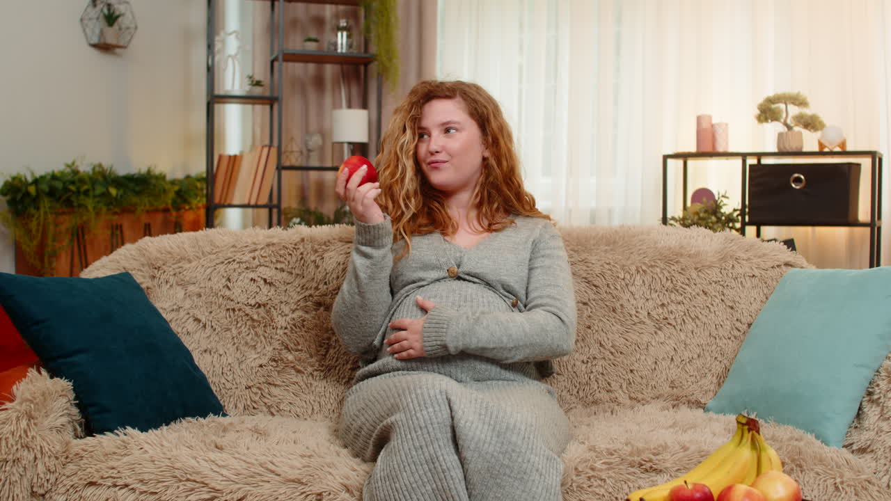 Pregnant woman eating apple gently touching belly relaxed with calm expression and healthy glow