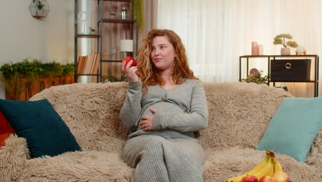 pregnant woman eating apple gently touching belly relaxed with calm expression and healthy glow