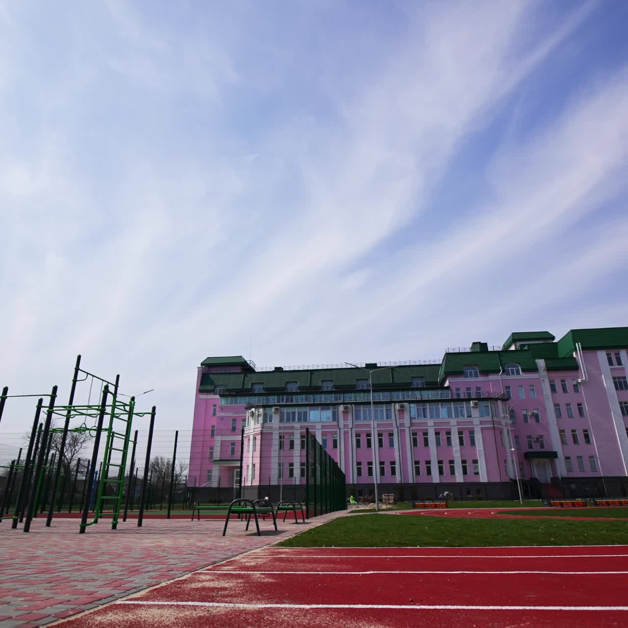Huge pink building with sports ground in front of it. Sports horizontal bars and red running track for sport activities. Low angle view