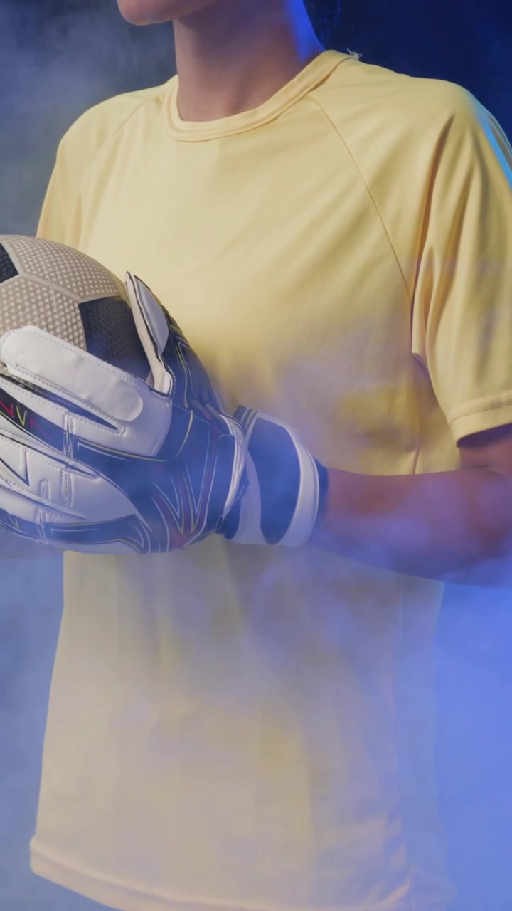 Video verticale: Telecamera in panoramica, portiere che tiene la palla e si gira in uno scatto in studio con guanti e maglia gialla.