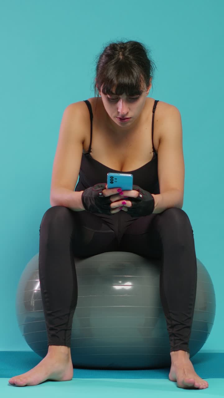 Woman using phone while sitting on exercise ball