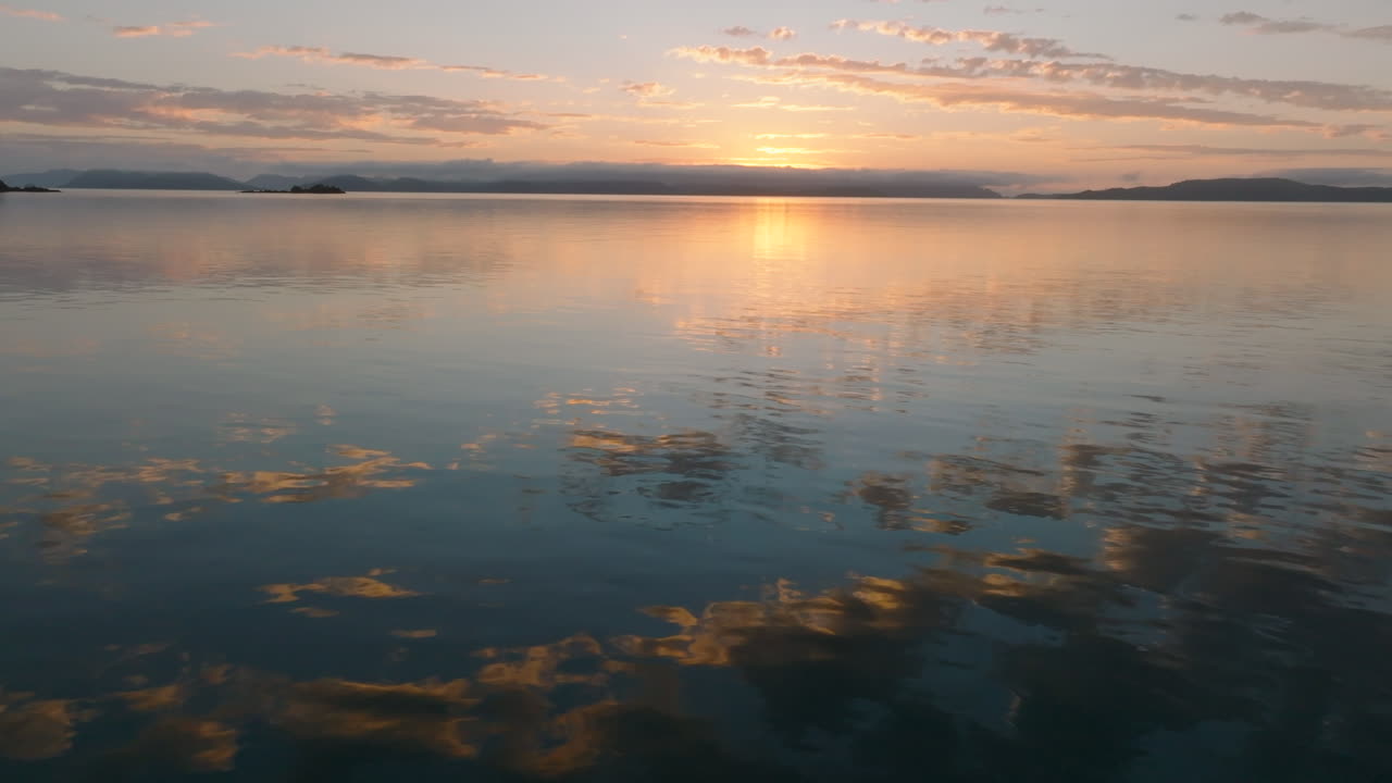 Drone flying low over the still ocean with the beautiful coloured sky and clouds reflecting on the water in the Whitsunday Islands during sunrise