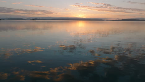 drone flying low over the still ocean with the beautiful coloured sky and clouds reflecting on the water in the whitsunday islands during sunrise