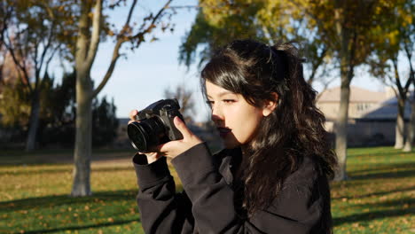 a beautiful woman model taking pictures with a professional digital mirrorless camera during a photo shoot in a park during autumn